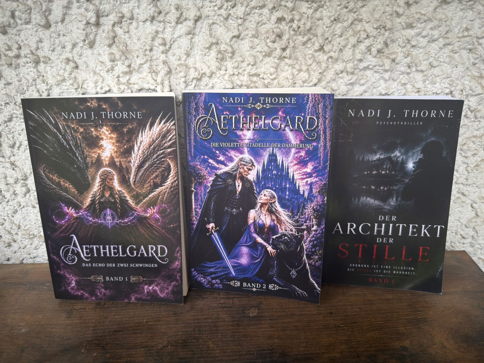 Die drei Taschenbücher von Nadi J. Thorne stehend nebeneinander: Aethelgard Band 1 und Band 2 sowie Der Architekt der Stille